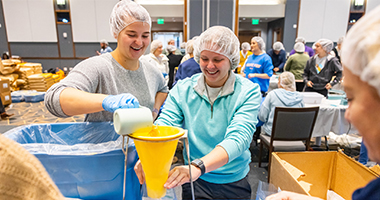 Two students help fill food portions while volunteering for the local food bank.