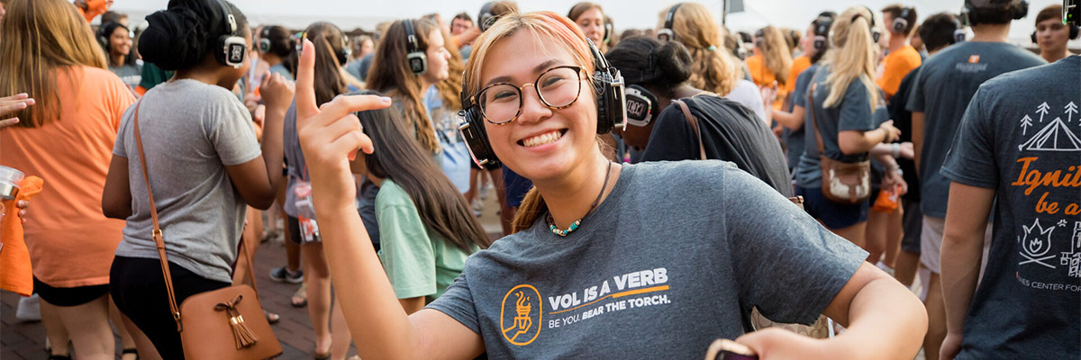 Asian girl wearing headphones smiles as part of a crowd enjoying the Silent Disco at UTK.