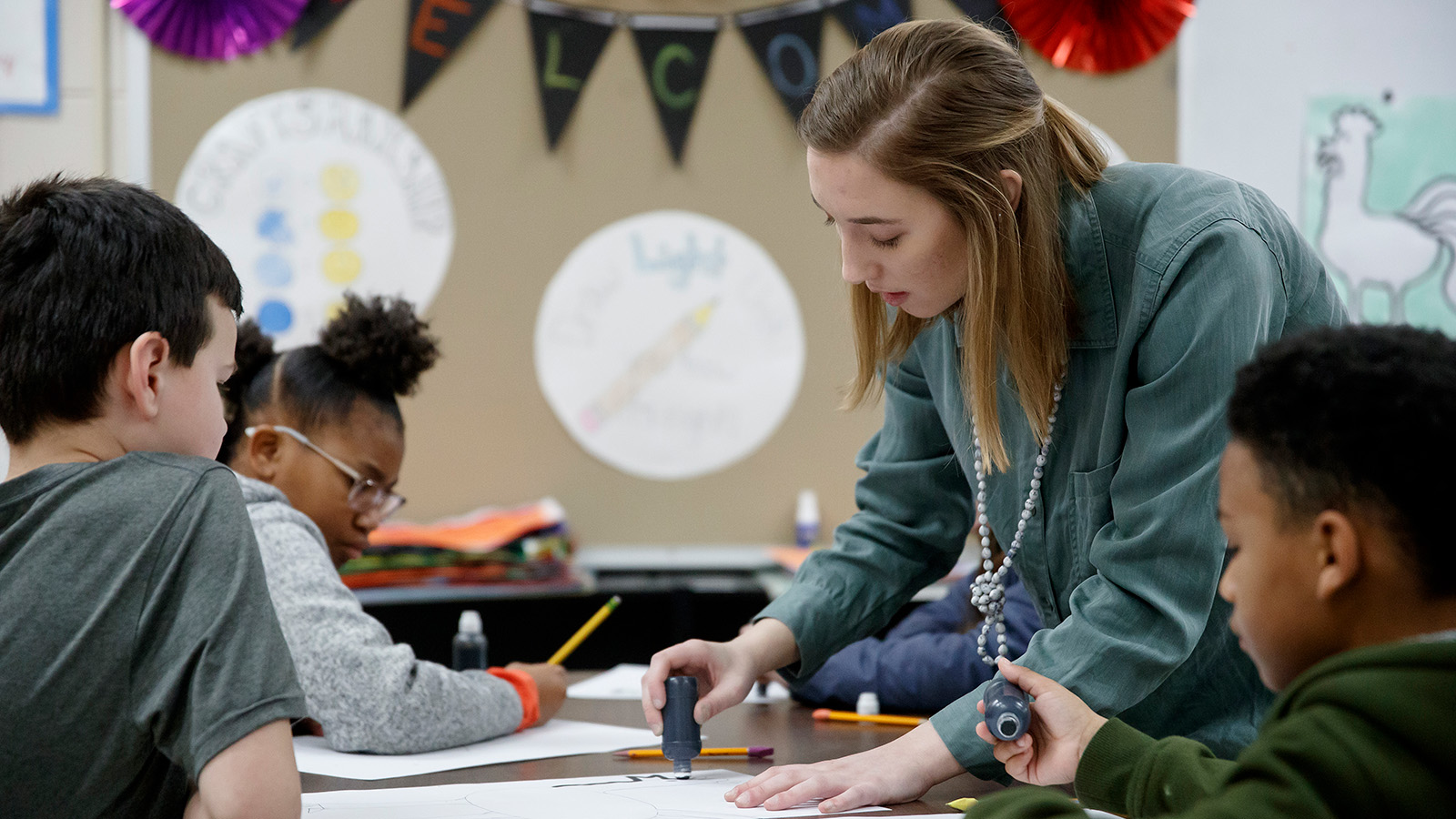 Teacher helping students in a class room with an assignment.