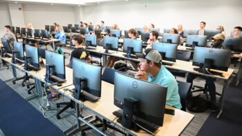 Students sitting in a classroom with desktop computers on the first day of class.