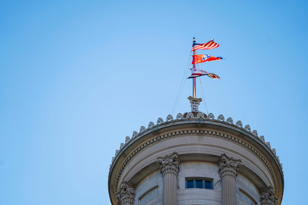 Top of a building with the American flag, the Tennessee state flag, and the flag of the Tennessee General State Assembly waving in the wind.