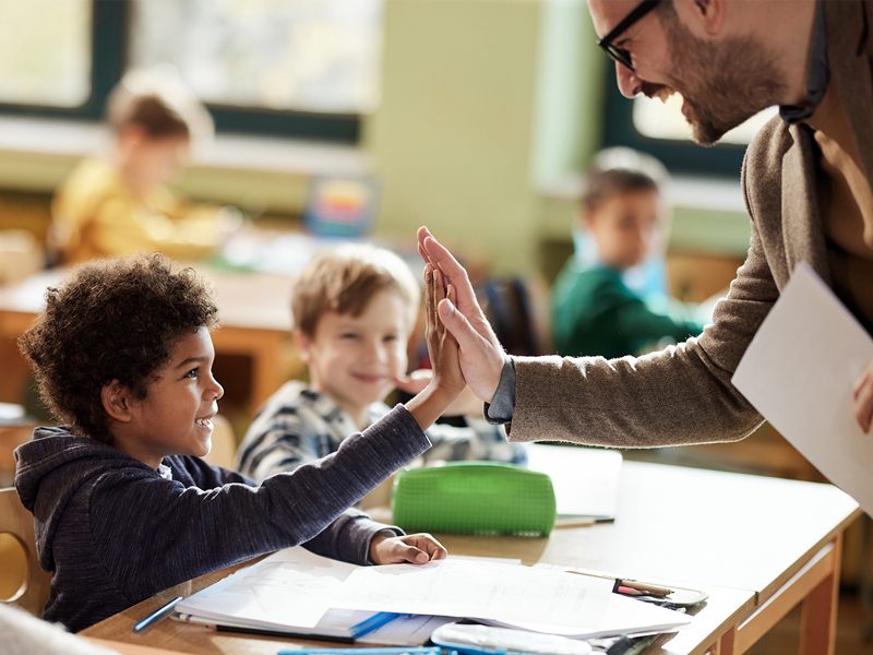 Happy male teacher giving high-fives to his elementary student in the classroom. Photo credit: Skynesher, iStock.com