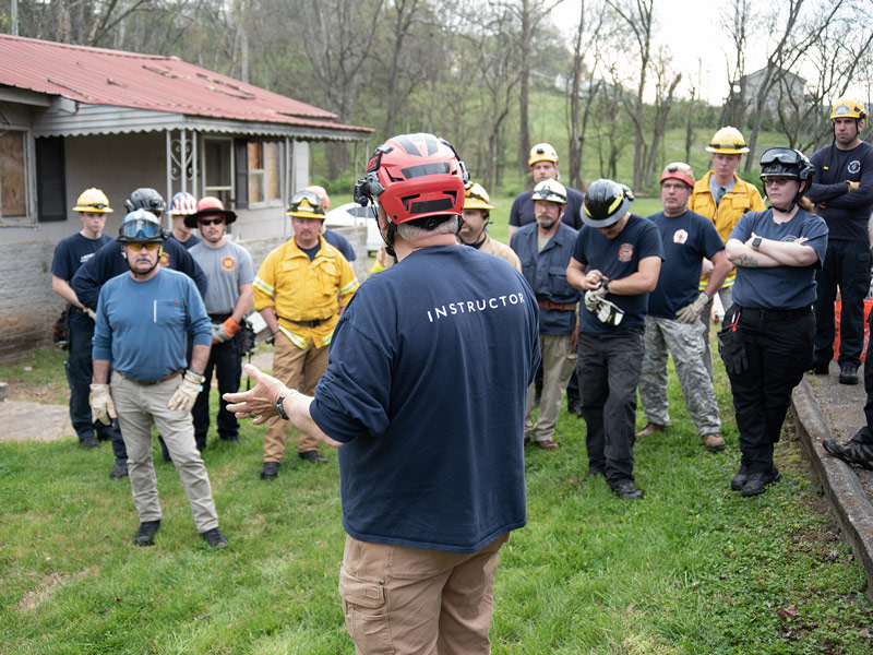 A group of first responder and emergency service workers listen to a demonstration during a training exercise.