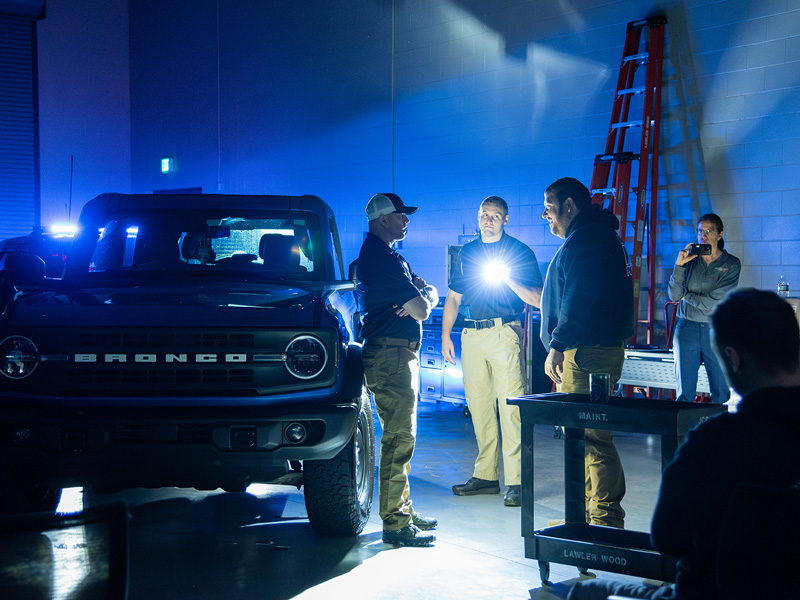 A group of people standing a dark room light by a bright flashlight, practicing law enforcement training.