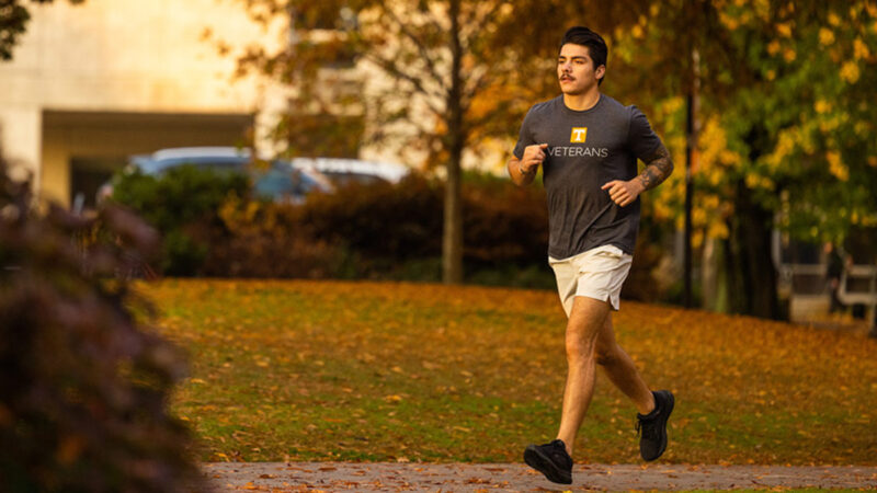 A young man with dark hair and mustache runs along a pathway during sunset.