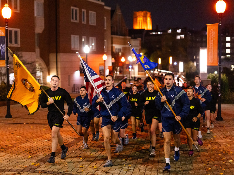 A group of ROTC cadets, all wearing their physical fitness uniforms, participate in a morale run, with guidon bearers in the front.