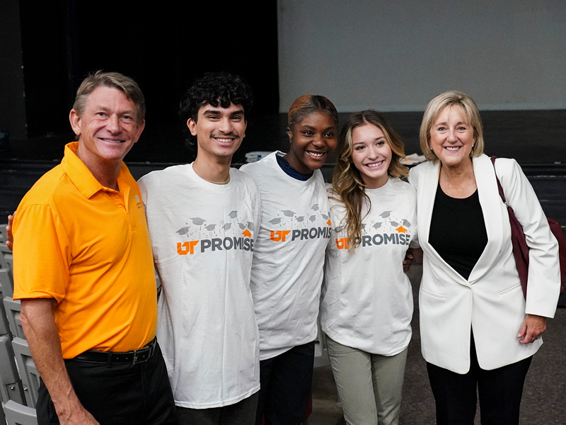 A man in an orange polo shirt standing with a group of four individuals wearing white shirts and jackets.