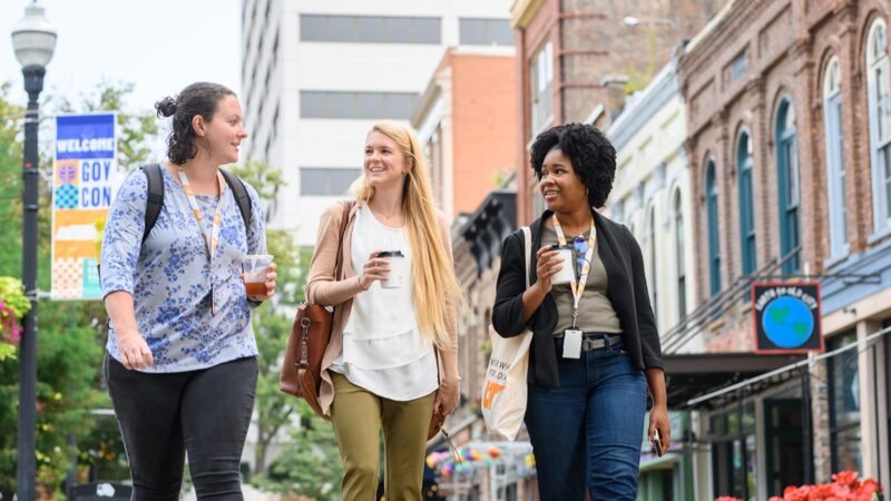 Three young women walking downtown while talking and holding coffee cups.