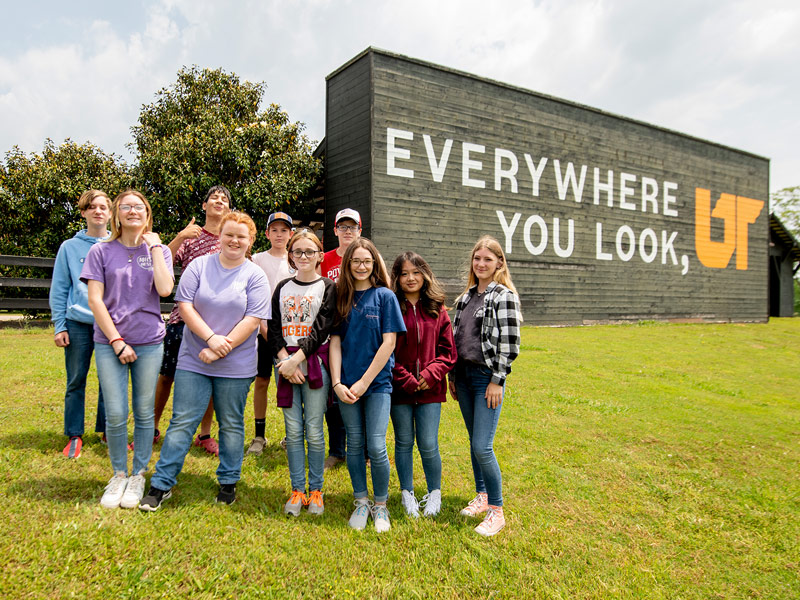 A group of children from a Tennessee 4-H camp pose for a photo in front of a building with "Everywhere You Look, UT" painted on it.