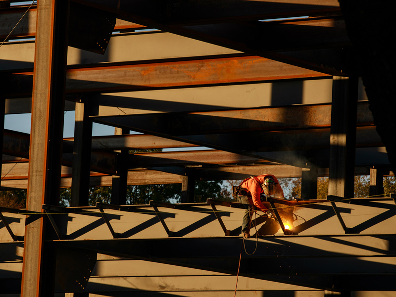 A construction worker sits on a steel beam while welding.