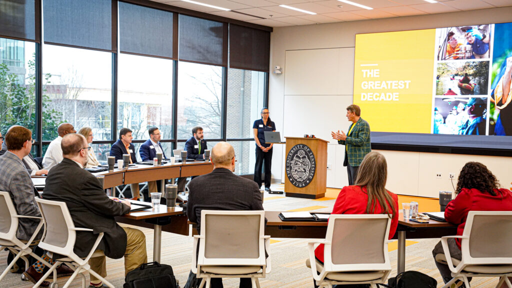 A group of people pose for a photo against an orange backdrop decorated with white and orange balloons.