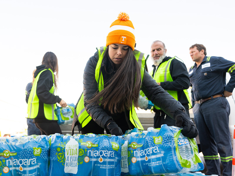 A group of UTK volunteers wearing yellow vests work to prepare bottled water donations for Hurricane Helene relief.