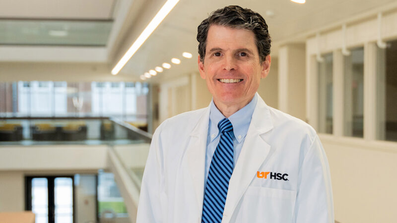 A smiling man wearing a white UT Health Science Center lab coat.