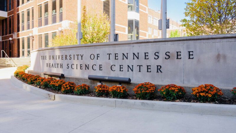 Large circular concrete flag base with metal lettering "The University of Tennessee Health Science Center", with orange flowers encircling the base.