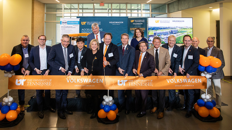 A large group of business men and women preparing to cut a large ribbon during a ceremony.