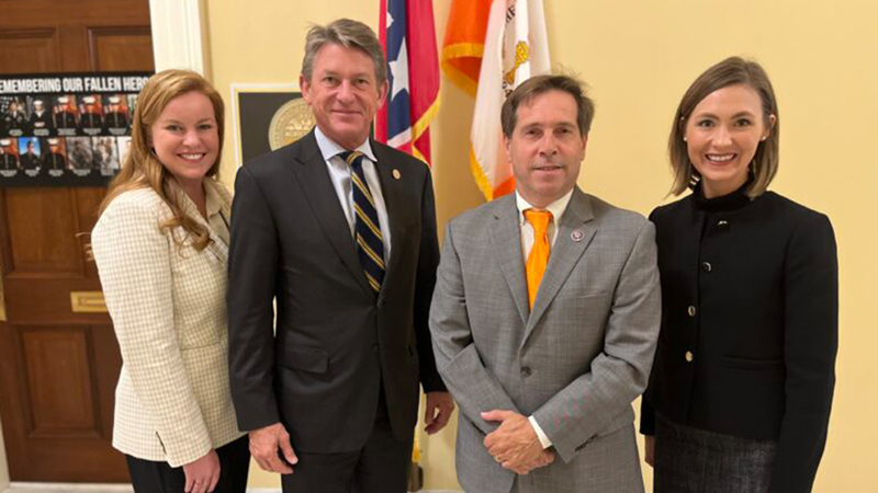 Two men and two women, all in business suits, standing for a group photo.