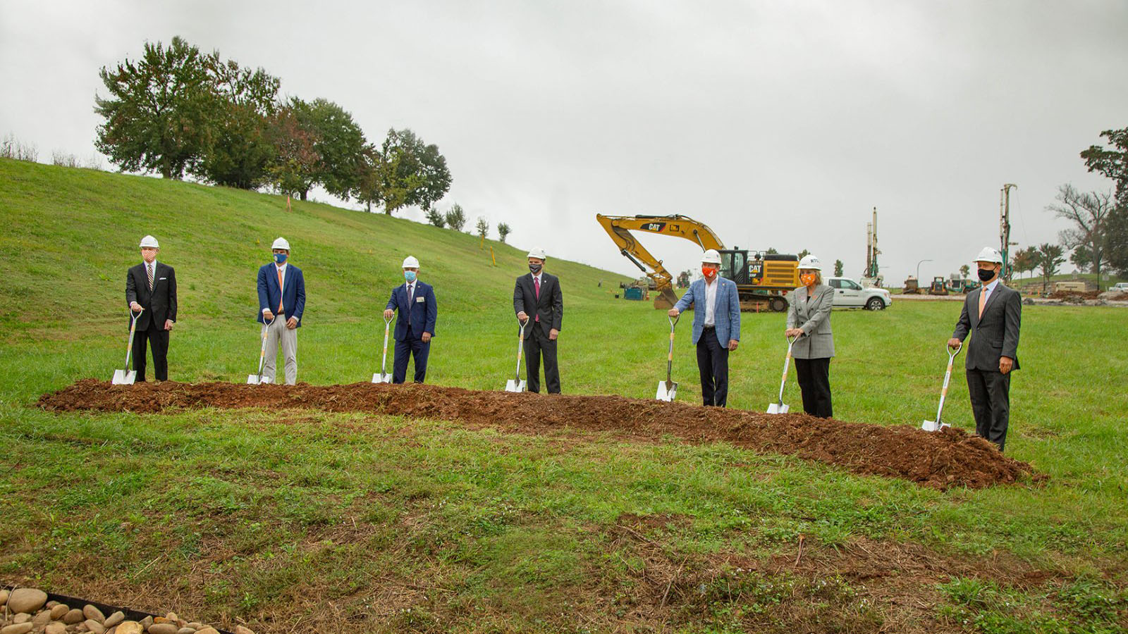 Seven people in hardhats pose with shovels in a groundbreaking event at Cherokee Farm|A rendering of a modern medical facility and office building