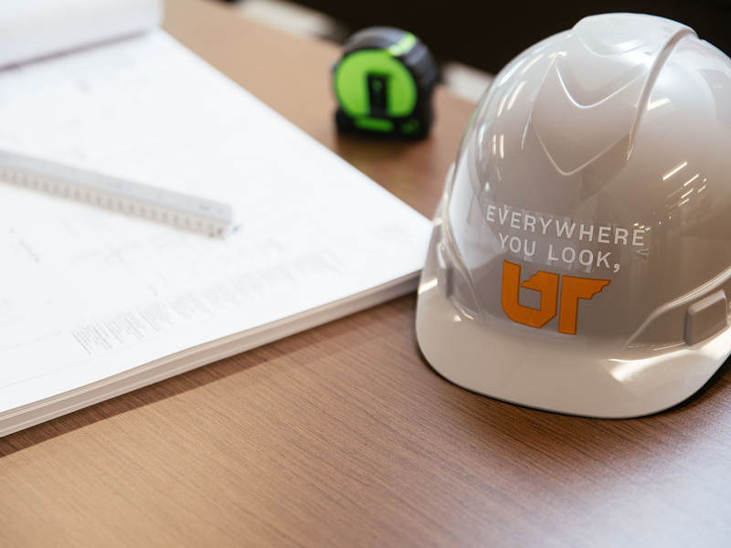 Hardhat with Everywhere You Look, UT logo and construction plans on a table.