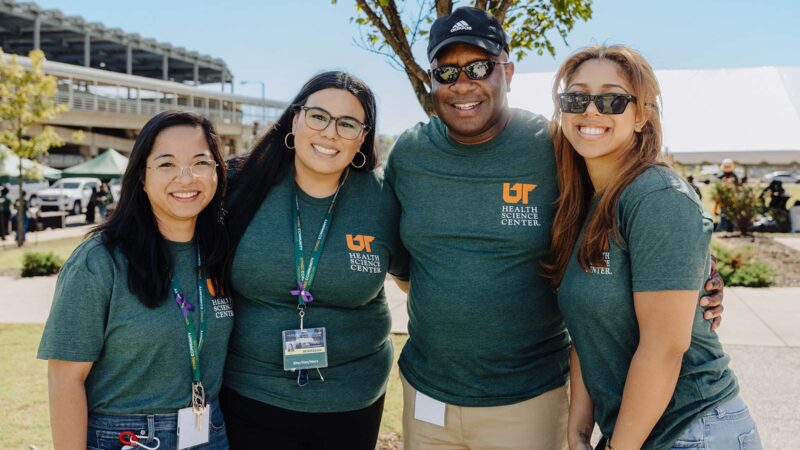 Three women and a man, all wearing green UTHSC shirts, stand together for a photo.
