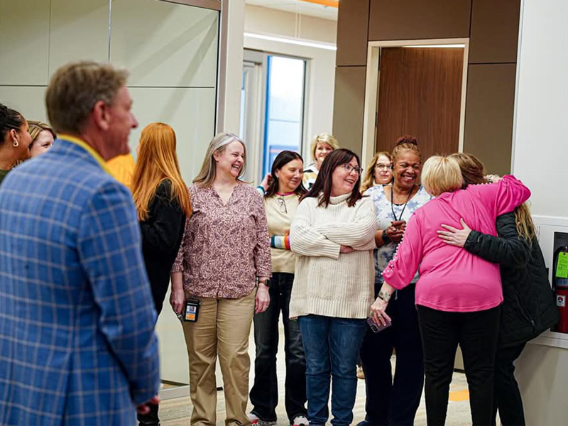 A group of employees smile and hug while talking with each other in a conference room.