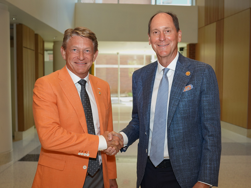 A man in an orange jacket and gray tie shaking hands while a man in a blue jacket and tie.