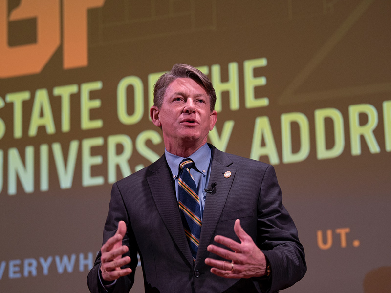 A man wearing a business suit and tie speaks to a crowd off-camera.