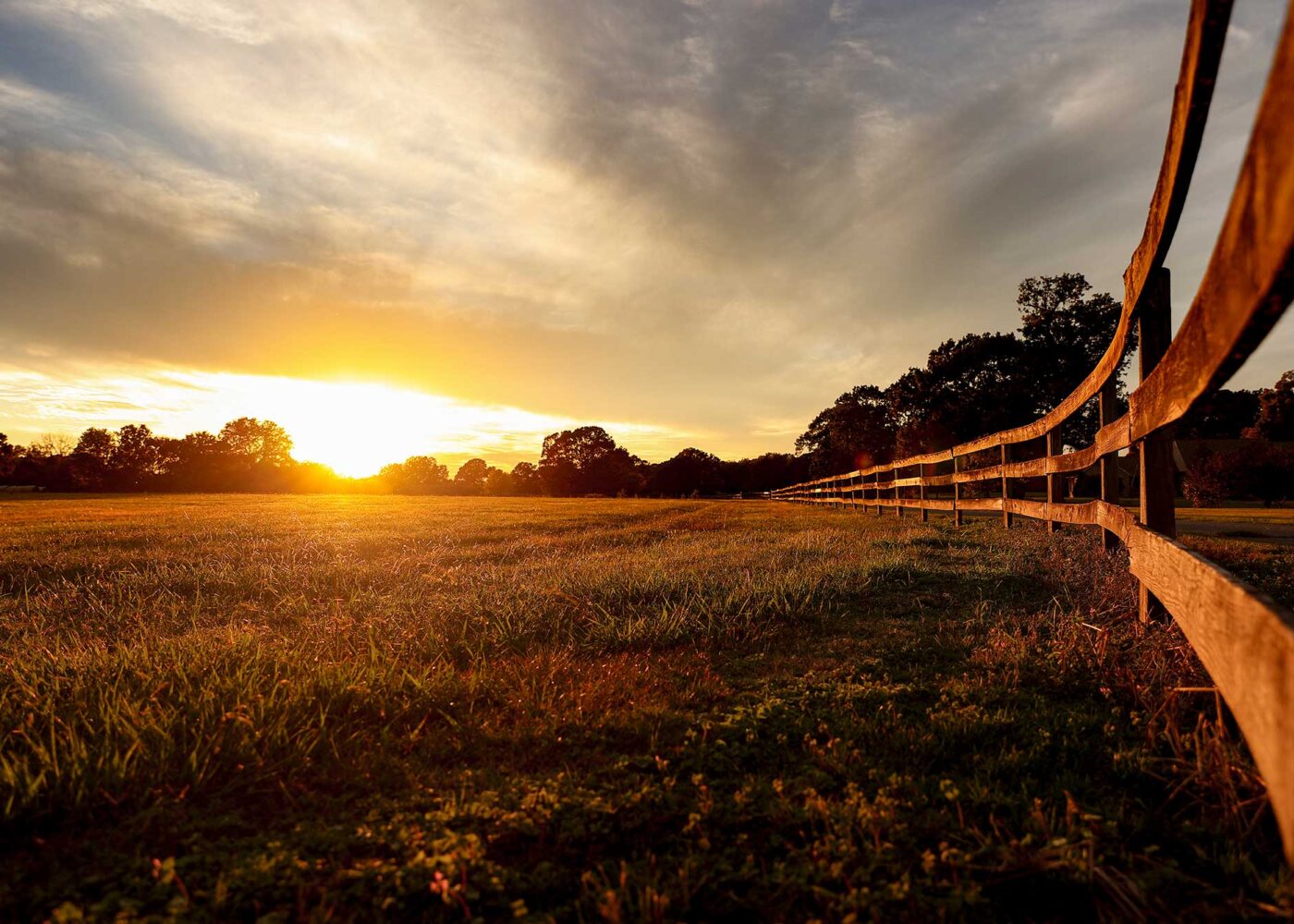 Sunset on a farm field, with a wooden fence running along the right side.