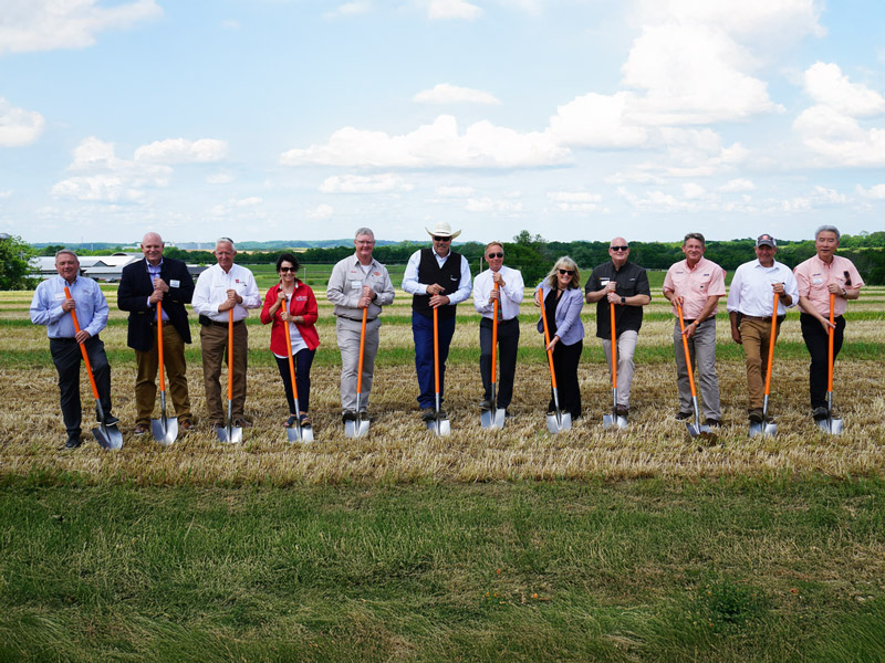 Several men and women holding shovels in an open grass field.