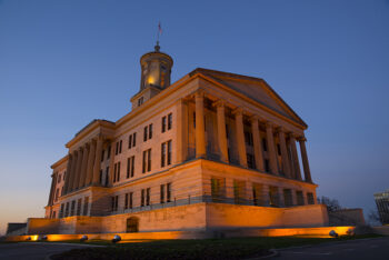 The Tennessee State Capitol building lit up by lights during a sunset.