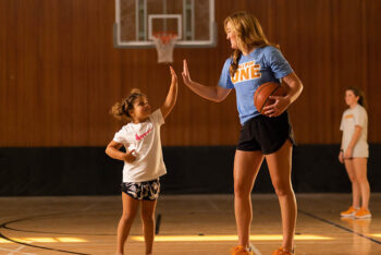 A college basketball player gives a young girl a high five on the court.