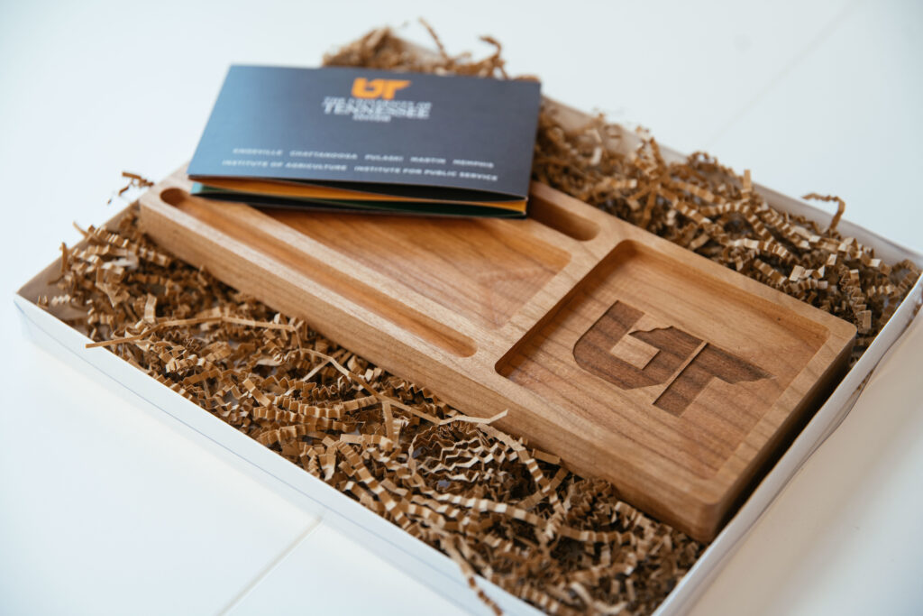 Wooden desk tray with space for holding a business card, nestled in a box of crinkle-cut paper.