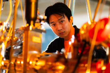 A young asian man working with a large piece of equipment in a lab.
