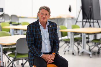 UT System President Randy Boyd sits on a stool in a classroom with this hands in his lap.
