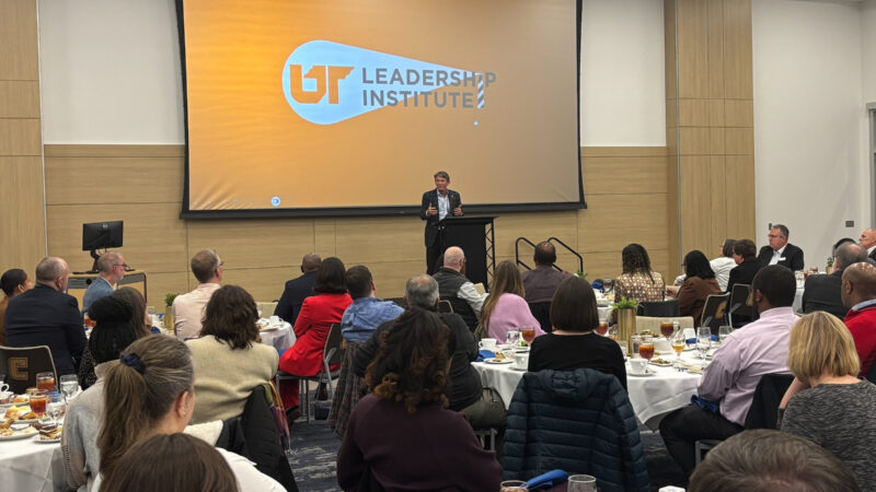 A crowd of employees listen from tables in a ballroom as UT System President Randy Boyd speaks from the podium during an event.