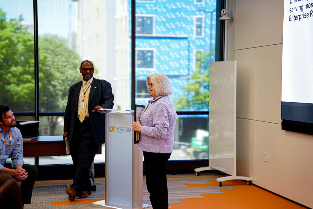A UT employee speaks from the podium while colleagues listen.