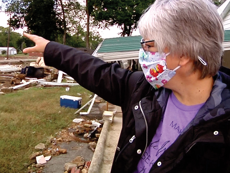 Debra Ashton points to damage in her front yard that marks the area where she was swept away by the flood waters.
