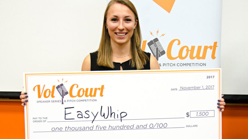 A young woman holds up a giant check representing her win of a entrepreneurial business competition.