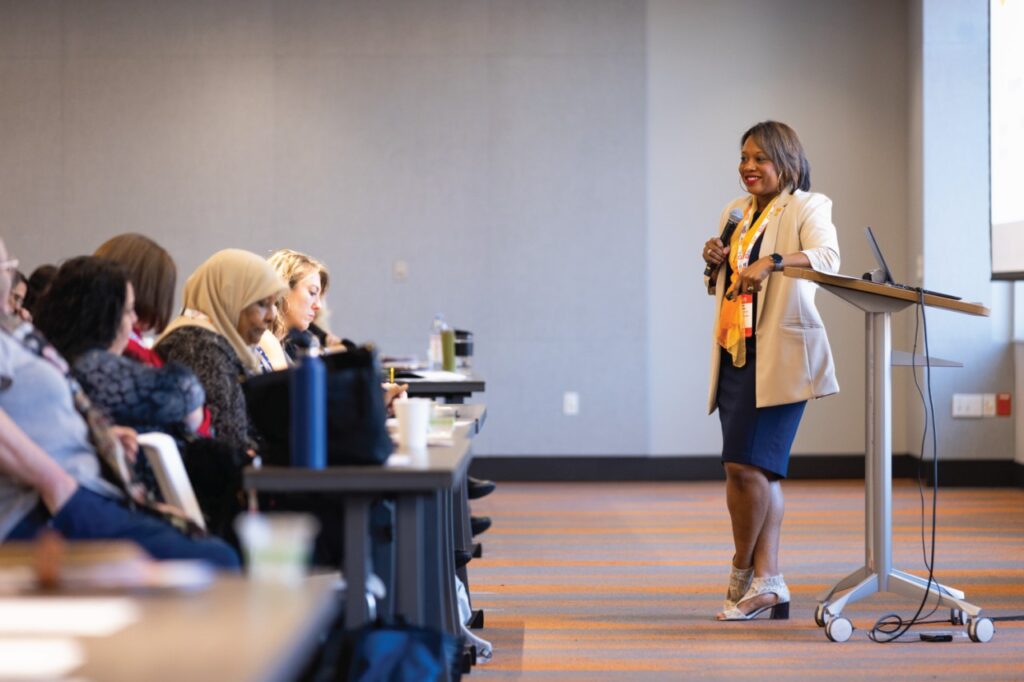 UT Knoxville Vice Provost for Student Success Amber Williams speaks to an engaged audience at a professional conference, standing beside a podium with a microphone in hand.