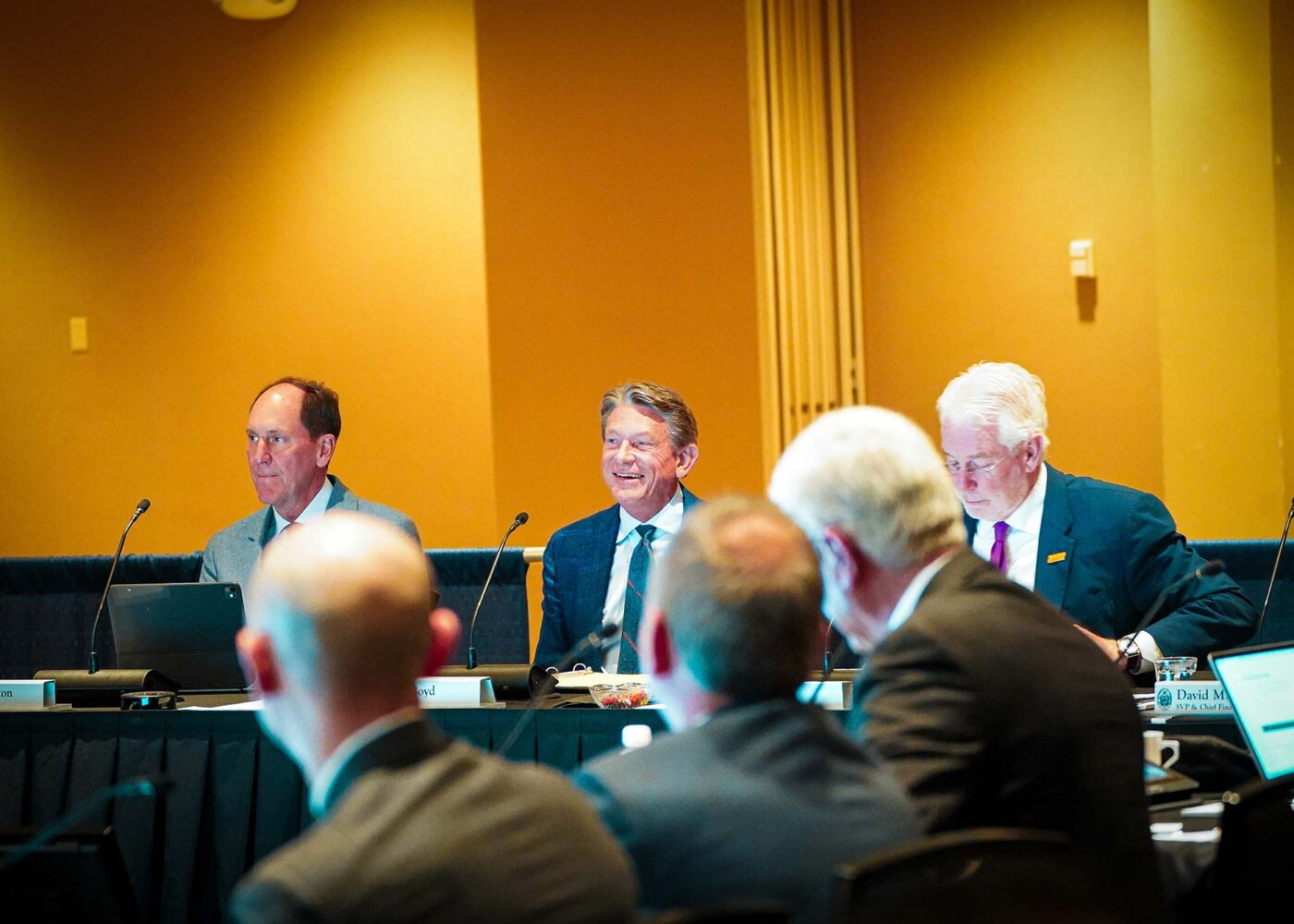 A group of men in business suits smiling and having a discussion during a board meeting.