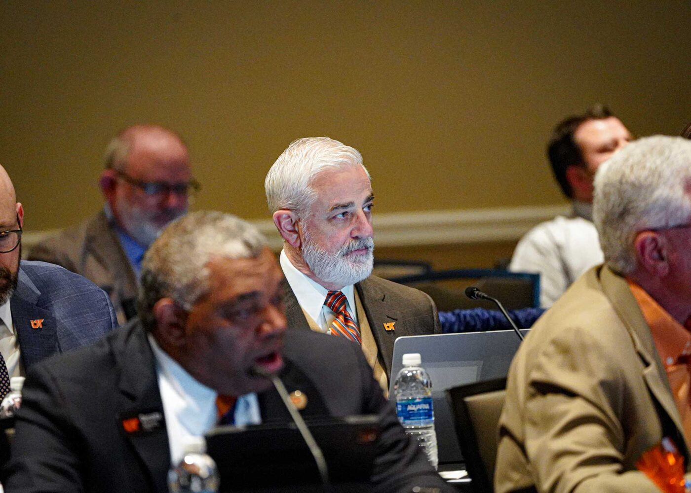 Several men in business suits listen intently during a board meeting presentation.