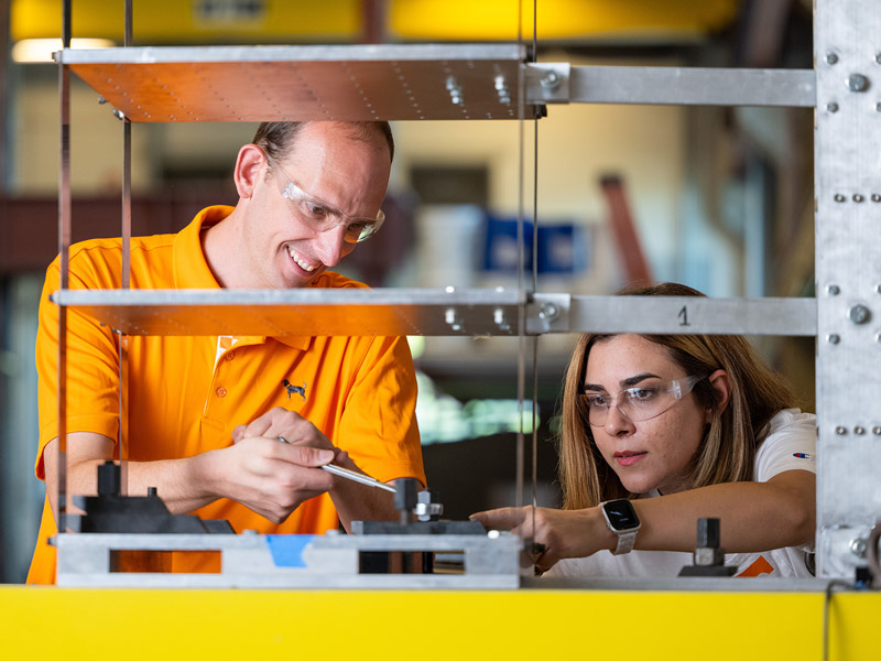 A man and woman work on a multi-level piece of table-top equipment.