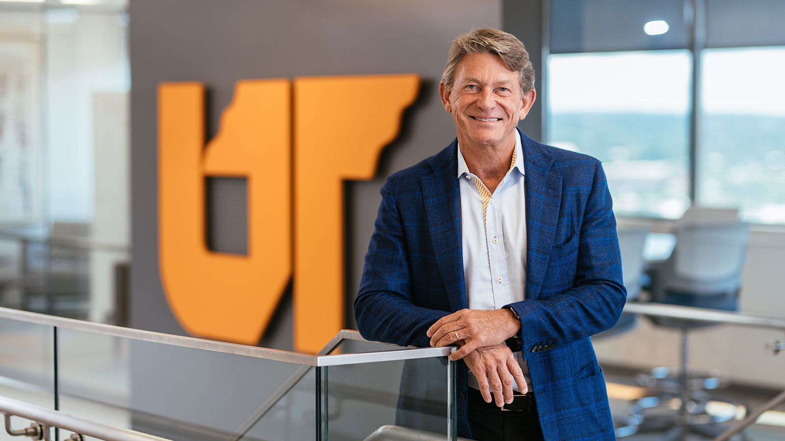 Randy Boyd resting with arms cross on a stairwell railing, with the UT icon behind him.