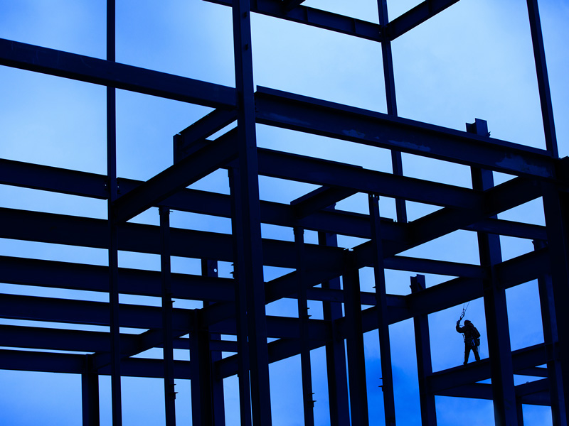Silhouette of the steel infrastructure of a building being constructed, against a bright blue sky in the background.