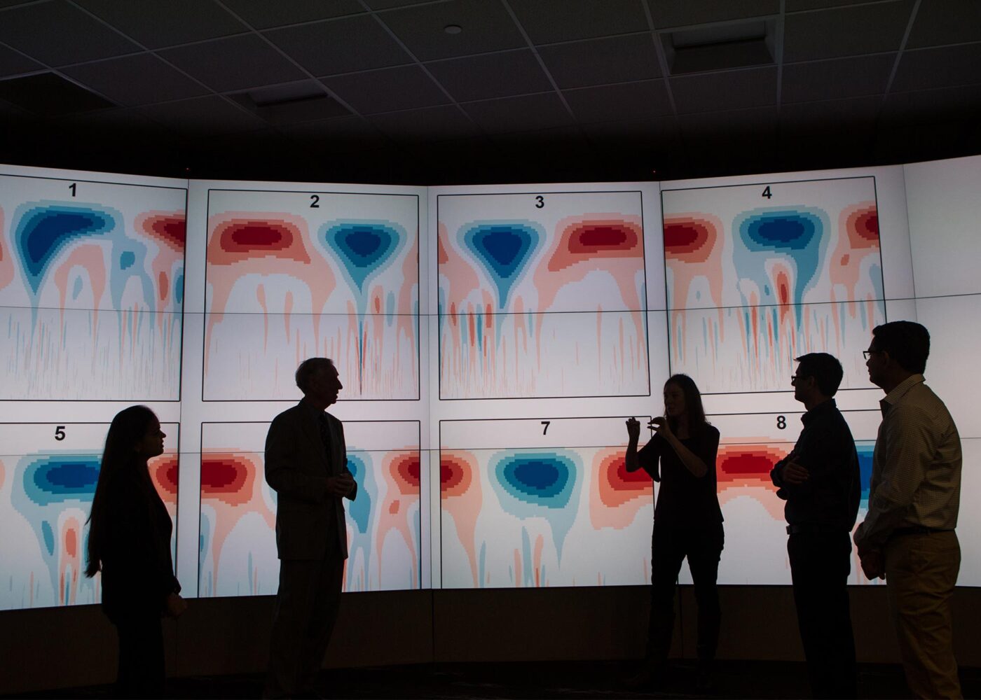 Silhouettes of several people looking at data on projected screens.