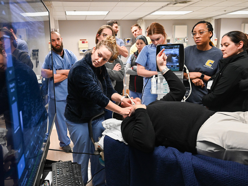 A group of medical students watch as one practices using a technique on an instructor.