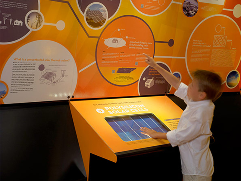 A child interacting with an orange-color exhibit from the Spectrum Solar Farm Exhibit.
