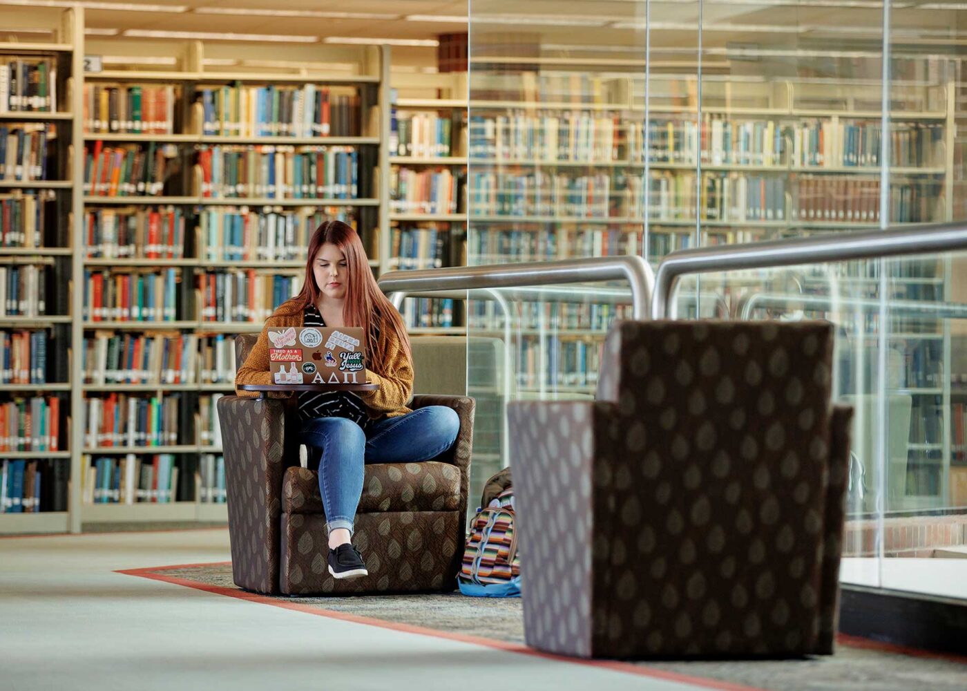 Young female student sitting in a library lounge area while working on her laptop.