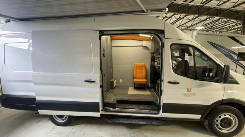 A white sprinter van is parked with its sliding door open, showing the interior, which serves as a mental health mobile clinic.