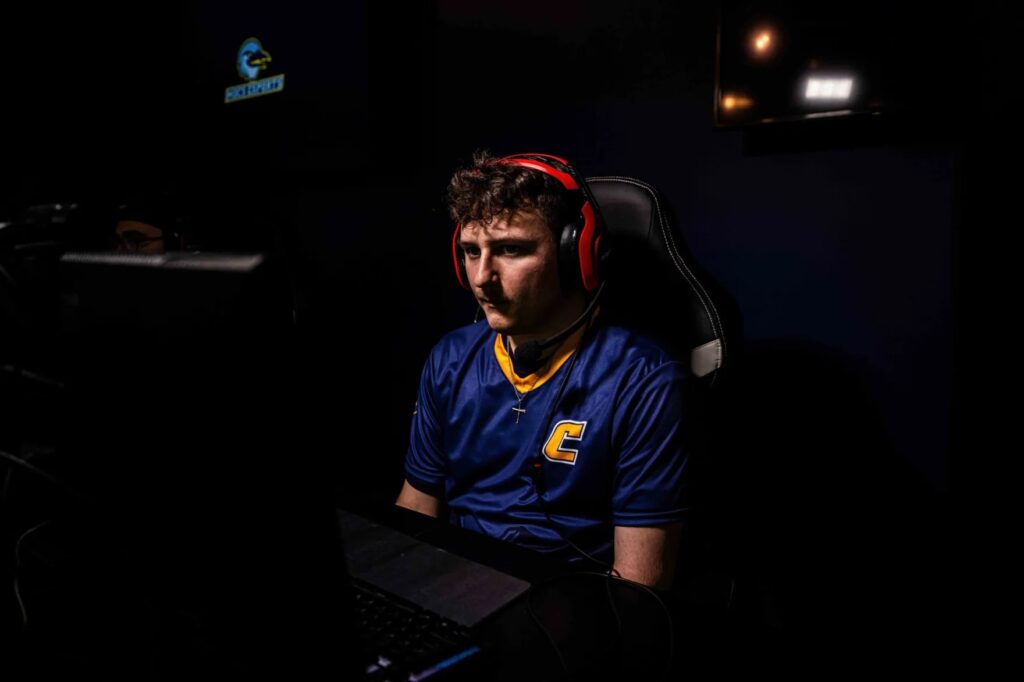 A UT Chattanooga student wearing a gaming headset focuses on a computer screen while competing in an esports match in a darkened gaming lab.