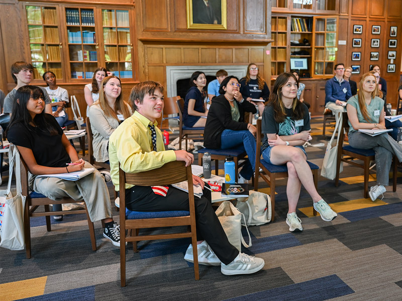 A group of students sitting and paying attention to a lecture inside a large room with wooden walls.
